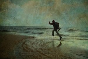 Man in raincoat jumping in water near ocean