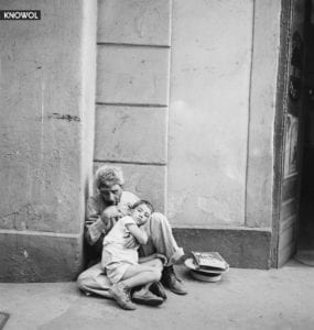 An older man, who seems to be a street beggar, sitting against a wall while cradling a poor child in San Juan, Puerto Rico.